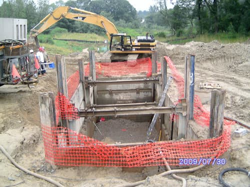 Excavator working a shored, safety-fenced excavation for an underground structure