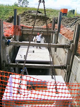 Precast concrete cover being set by crane into a shored pump station excavation